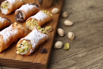 Delicious cannoli with ricotta cheese, peanuts, pistachios, chocolate and powdered sugar on wooden table, closeup. Space for text