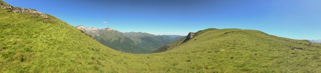 Fototapeta premium Panoramic view of lush green highlands with distant mountains under clear skies