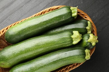 Fresh ripe zucchinis in wicker basket on black table, top view