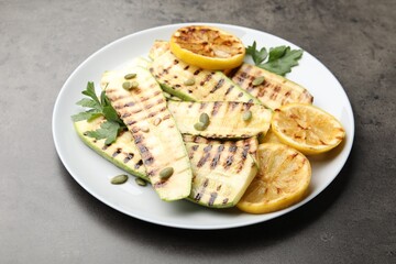 Delicious grilled courgette slices with pumpkin seeds, lemon and parsley on grey table, closeup