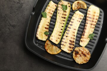 Delicious grilled courgette slices with garlic, lemon and parsley in pan on grey textured table, top view