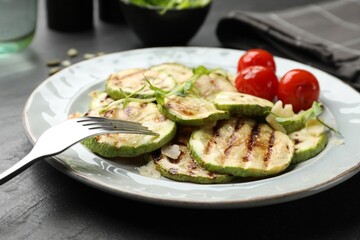 Delicious grilled courgette slices with tomatoes and microgreens served on black table, closeup