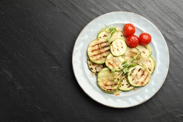 Delicious grilled courgette slices with tomatoes and microgreens on black textured table, top view. Space for text