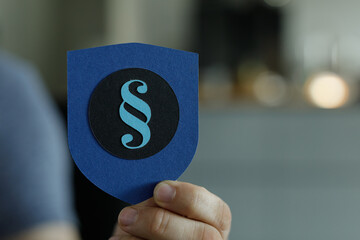 Image of a hand holding a blue shield with a paragraph symbol, representing legal protection and...
