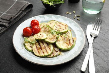 Delicious grilled courgette slices with tomatoes and microgreens served on black textured table, closeup