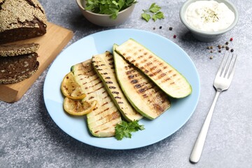 Delicious grilled courgette slices with parsley and lemon served on gray textured table, closeup