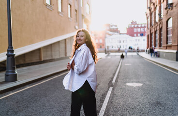 Smiling woman outdoors in white shirt, enjoying sunset on urban street. Conceptual photo...