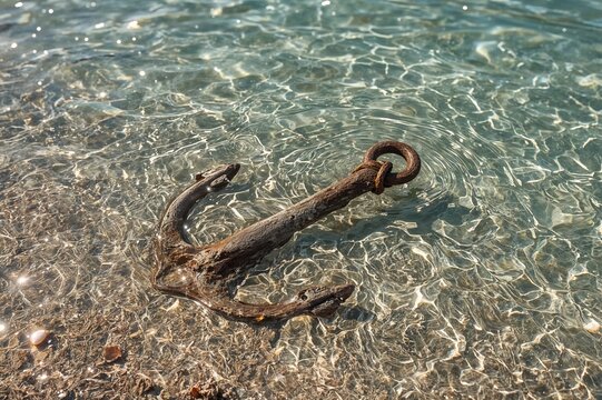Rusty anchor rope with metal snap hook submerged underwater near sandy ocean floor