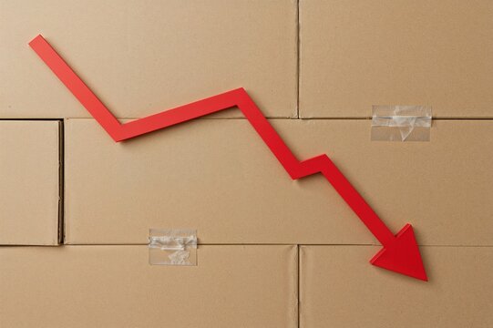 Declining sales and production shown by cardboard boxes and a red arrow pointing downwards. Economic downturn and reduced business operations.