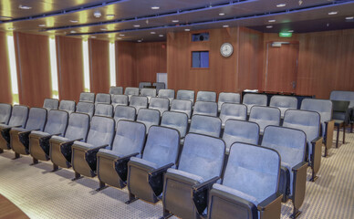 Naklejka premium Classic movie theatre lecture room lounge onboard small cruiseship cruise ship liner with movie screen and plush armchairs seating in intimate red velvet elegant ambiance decor