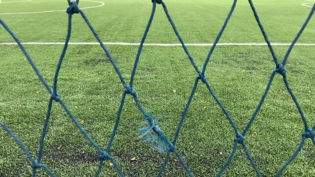 A mesh rope fence stretches across the frame, with a football field visible in the background, symbolizing boundaries, focus, and sporting atmosphere. 4k video footage.