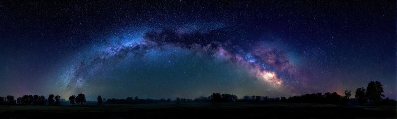 Fototapeta premium Panoramic view of a night sky filled with the Milky Way galaxy, silhouetted trees along a horizon