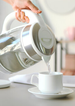 Pure water boils in an electric kettle on the table in the kitchen. Vertical photo format