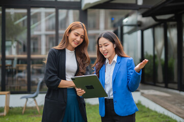 Fototapeta premium Asian businesswoman using digital laptop while standing in front of modern building. Attractive female employee working in front of office.