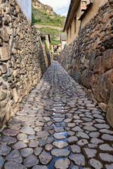 Traditional narrow alleyway with ancient Inca stone walls and cobblestone pavement in the historic town of Ollantaytambo, Peru.