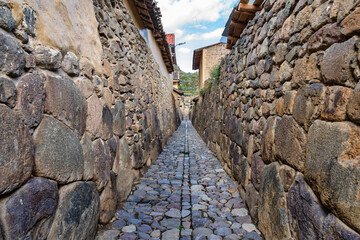 Traditional narrow alleyway with ancient Inca stone walls and cobblestone pavement in the historic town of Ollantaytambo, Peru.