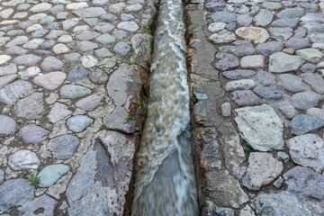 A traditional cobblestone street with a flowing Inca water canal in Ollantaytambo, Sacred Valley, Peru