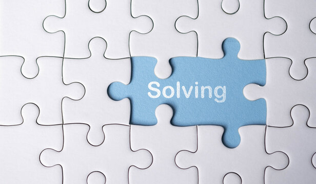 Puzzle pieces coming together with a blue piece that says Solving symbolizing finding solutions, completing tasks, critical thinking, teamwork, and strategic problem-solving.