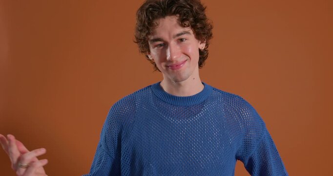 Reveal video clip of a young adult male smiling while gesturing towards the camera in the studio. He has dark curly hair and is wearing casual clothing.