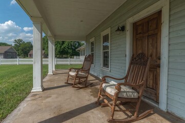 A pair of vintage rocking chairs sit on the porch of a weathered home