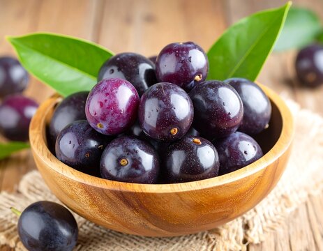 A close-up of fresh, ripe Java plums, also known as Jamblang or Syzygium cumini, overflowing from a rustic wooden bowl with green leaves