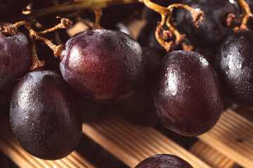 Bunch of fresh purple grapes on a black plate, placed on a wooden base, with a rustic background. Natural style image, ideal for concepts of healthy eating, fruits, nutrition and gastronomy.