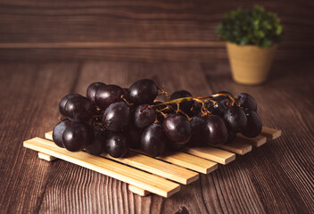 Bunch of fresh purple grapes on a black plate, placed on a wooden base, with a rustic background. Natural style image, ideal for concepts of healthy eating, fruits, nutrition and gastronomy.
