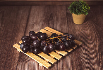 Bunch of fresh purple grapes on a black plate, placed on a wooden base, with a rustic background. Natural style image, ideal for concepts of healthy eating, fruits, nutrition and gastronomy.