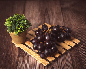 Bunch of fresh purple grapes on a black plate, placed on a wooden base, with a rustic background. Natural style image, ideal for concepts of healthy eating, fruits, nutrition and gastronomy.