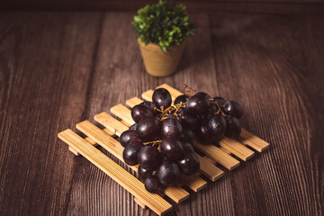 Bunch of fresh purple grapes on a black plate, placed on a wooden base, with a rustic background. Natural style image, ideal for concepts of healthy eating, fruits, nutrition and gastronomy.
