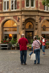 Obraz premium Group of three older adults standing on a town square near a flower shop and historic building, observing the surroundings.