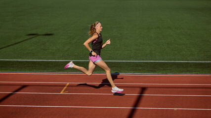 Obraz premium Female athlete running on a track under clear skies during daytime training session. Concept of sprinting, acceleration, explosive power, athletic progress, competition energy.