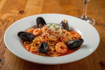 Seafood penne served on a dish at the dining table, featuring mussels, squid, tomatoes, and grated cheese up close