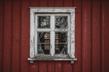 A weathered window with peeling white paint reveals a view into the history of a red structure, its cracked glass capturing the ambient light and suggesting untold tales inside.