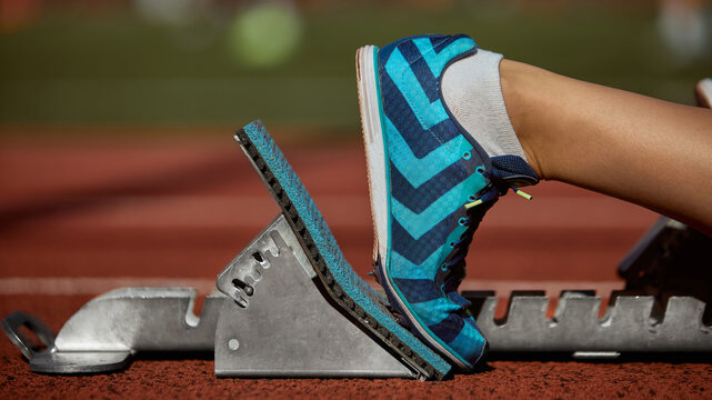 Runner preparing to start race with foot on starting block on track in warm sunlight. Concept of athletics detail, professional sports equipment, race preparation, focus, and competitive readiness.