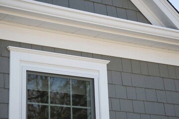 White soffit ensuring excellent airflow for roof eaves, crown molding detail above window, white trimboard, natural wood-effect vinyl, gray shingle siding on a newly built house