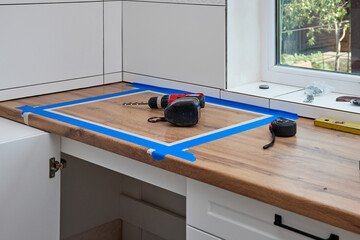 red cordless electric drill screwdriver and measuring tape on kitchen countertop. Kitchen cabinet installation