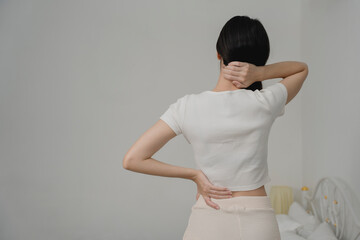 Rear view of woman touching her neck and lower back, indicating pain or muscle strain. Ideal for health issues, body discomfort, physical therapy, posture problems, and wellness awareness content.