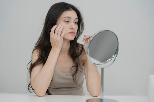 Woman looking at herself in mirror while touching her face, concerned about skin problems or imperfections. Ideal for skincare, beauty routine, acne, and personal health awareness content.