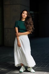 Fototapeta premium Stylish young asian female in green top and white skirt standing outdoors
