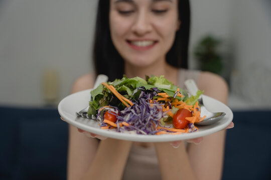 Close-up of colorful fresh salad on plate held by smiling woman, healthy meal with vegetables and greens. Concept of healthy eating, vegan lifestyle, plant-based diet, wellness, and clean food.