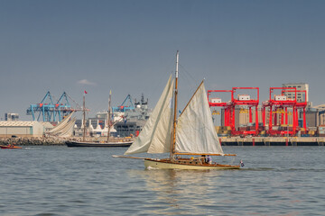 Tall ships sail on the River Mersey during a maritime event in Liverpool, England, with industrial structures in the background.
