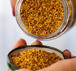 A jar of bee pollen is poured onto a plate. Colorful and natural bee pollen granules.