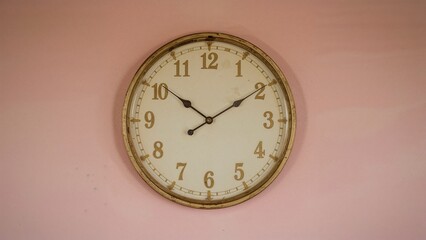 Retro styled white metal clock displaying time against a soft pink weathered wall, vintage concept, grunge effect, clock face and hands