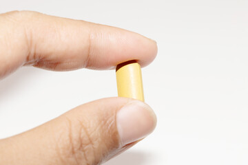 Close-up of a male hand gently holding a single yellow vitamin pill against a clean white background, symbolizing health and daily supplements.