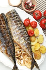 Tasty roasted mackerels with spices, tomatoes and potatoes on table, flat lay. Homemade seafood dish