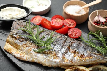 Tasty roasted mackerel served with spices and sauce on black table, closeup. Homemade seafood dish