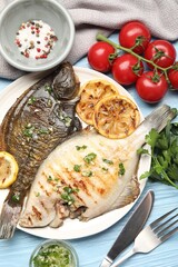 Tasty roasted flounder fish with herbs and lemon slices served on light blue wooden table, flat lay. Homemade seafood dish