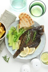 Tasty roasted flounder fish with celery served on white table, flat lay. Homemade seafood dish
