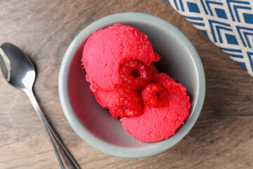 Delicious raspberry sorbet with fresh berries in bowl and spoon on wooden table, flat lay